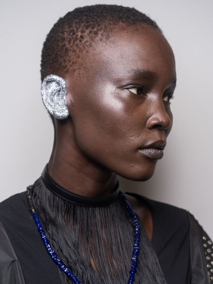 A close-up of a model's glitter ear backstage at the Toga S/S 27 show