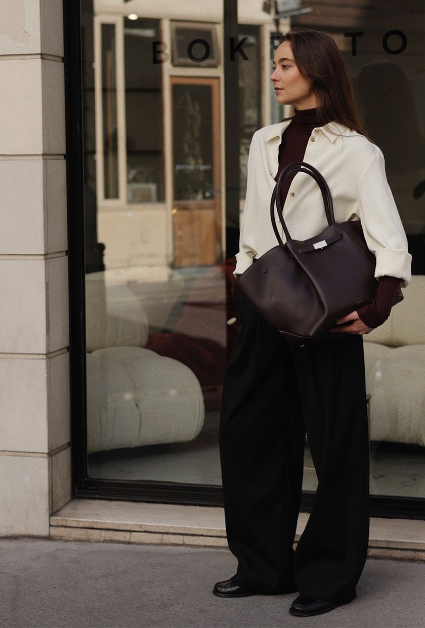 A woman in the street wearing a white button-down over a red turtleneck, styled with black trousers, black loafers, and a red bag.