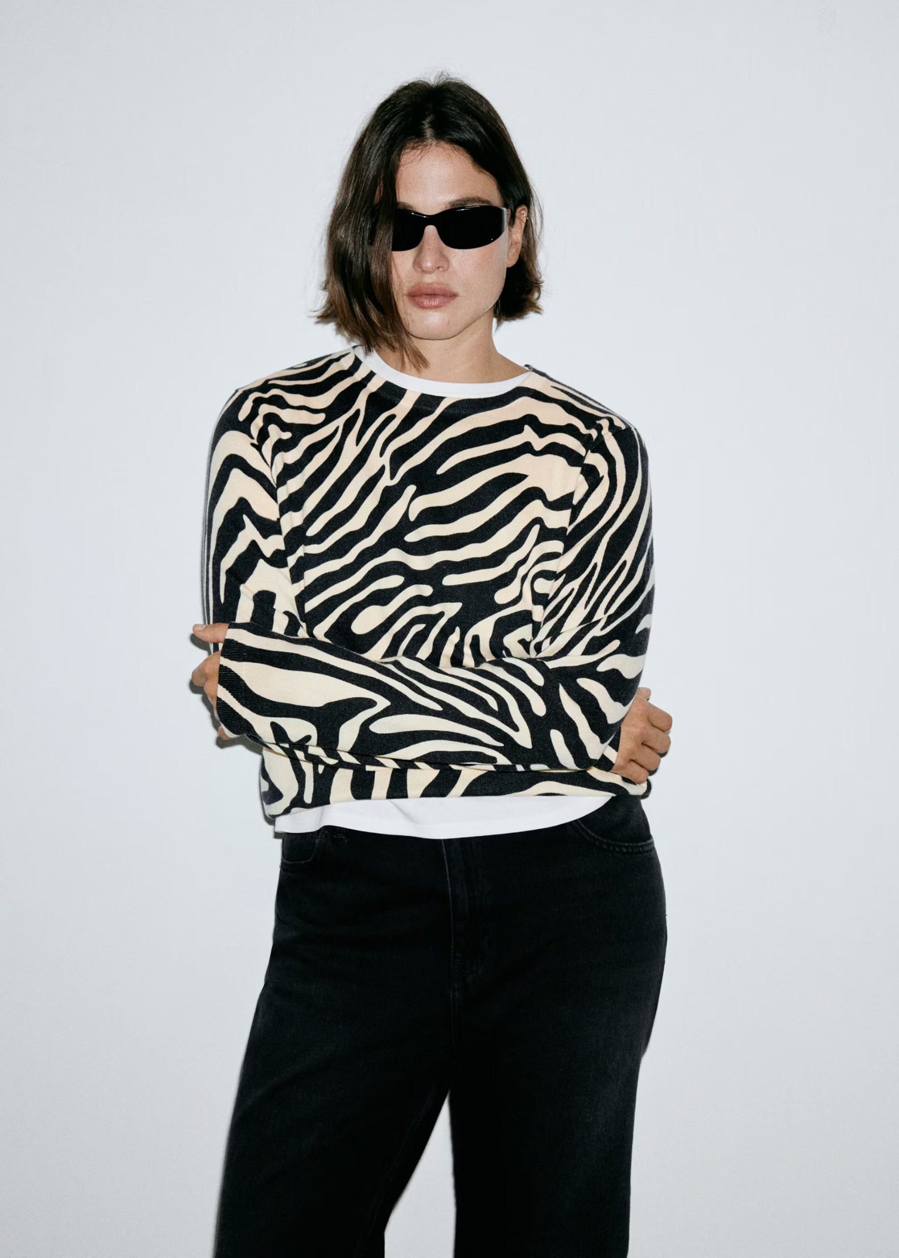An image of a model wearing a fine knit zebra jumper with black trousers and sunglasses