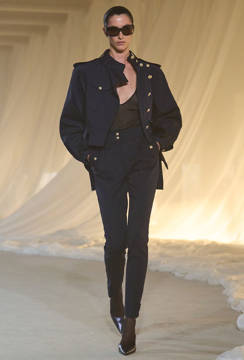 Balmain F/W 26 model wearing a navy jacket with a sheer tank and skinny trousers.