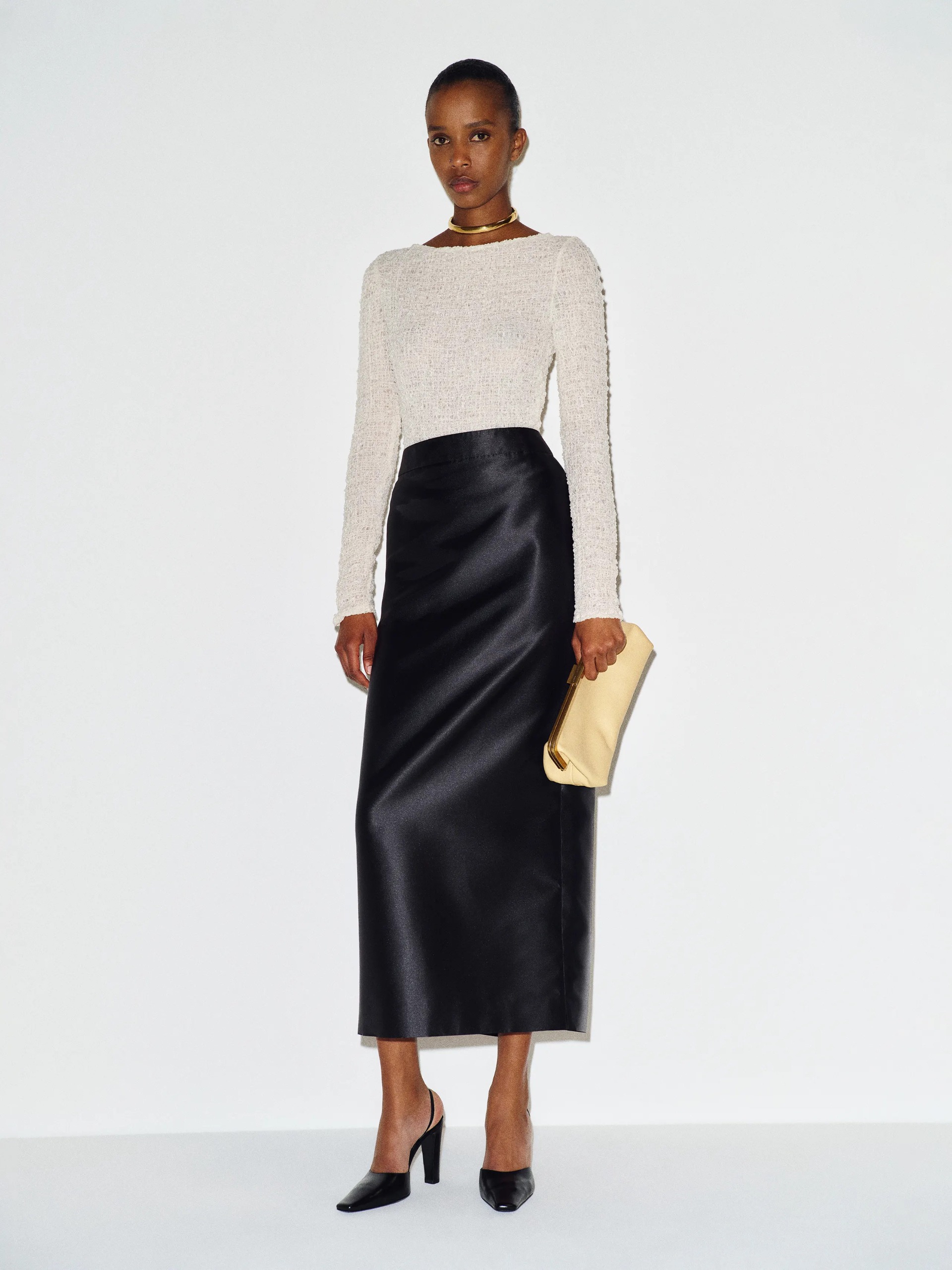 A model wearing a satin black maxi pencil skirt with a white long-sleeve shirt and black heels