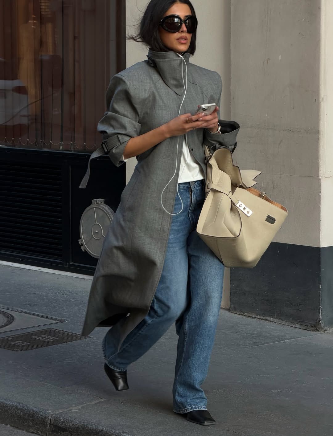 An image of @sherienboni  wearing a grey trench coat with blue jeans.