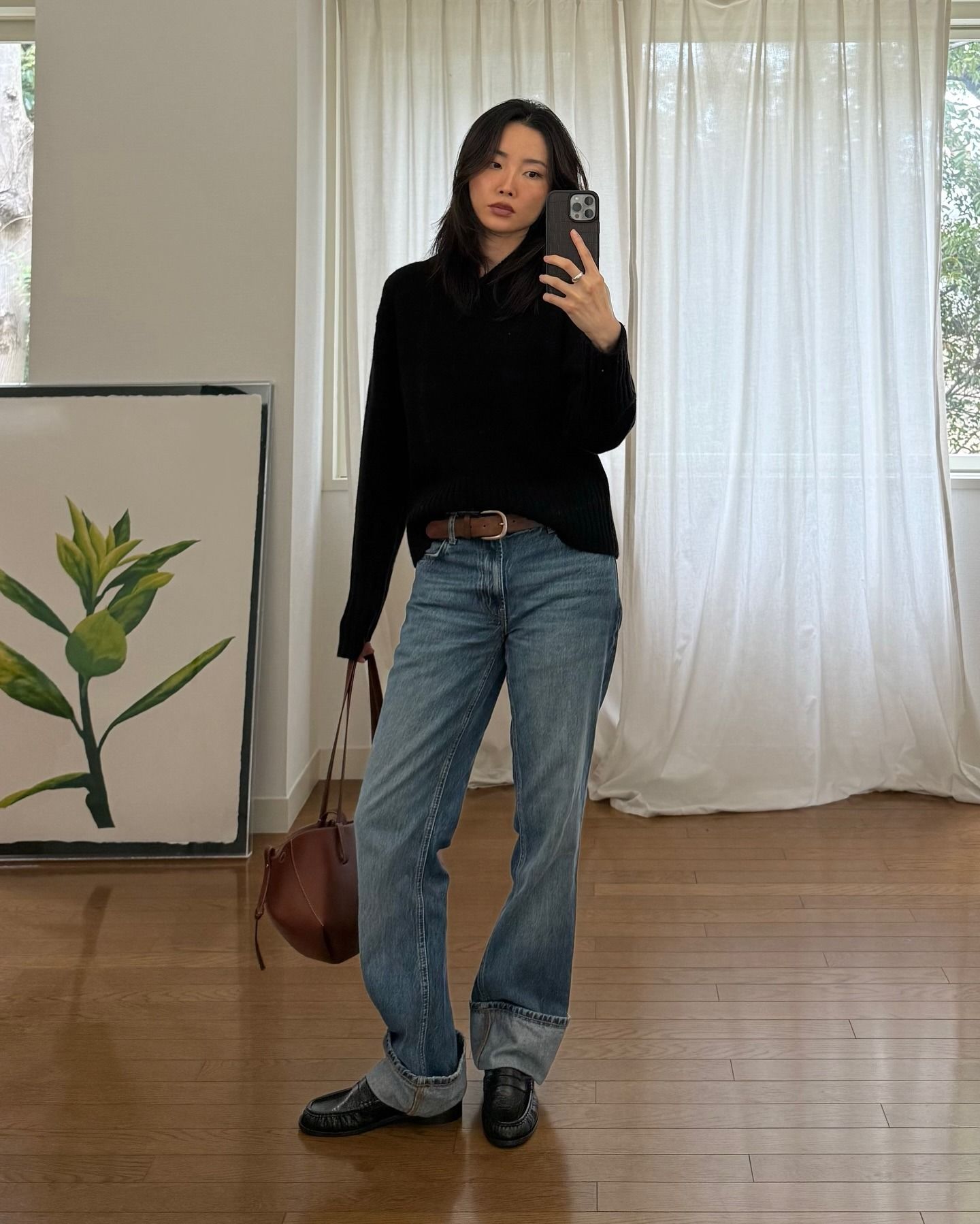 Woman wears black v-neck jumper, blue jeans, loafers, brown belt