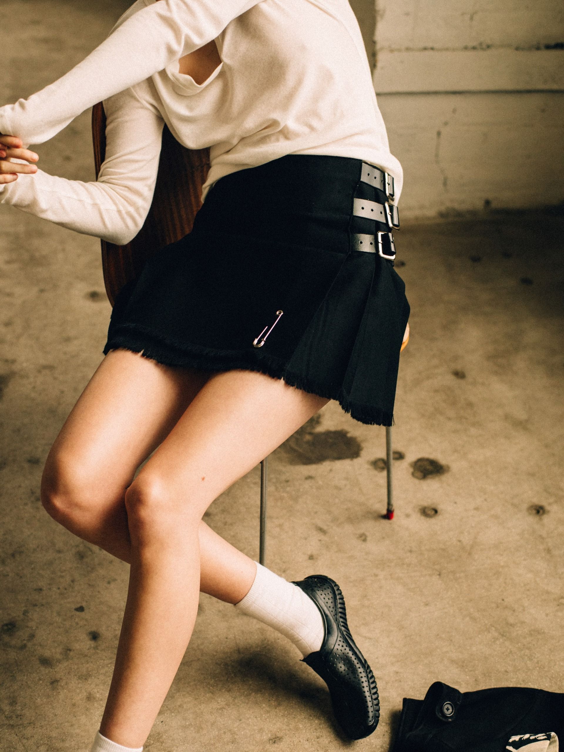 how to wear a kilt in 2026:Le Kilt campaign imagery shows a model wearing a cream longsleeve top, black, kilt skirt and leather loafers