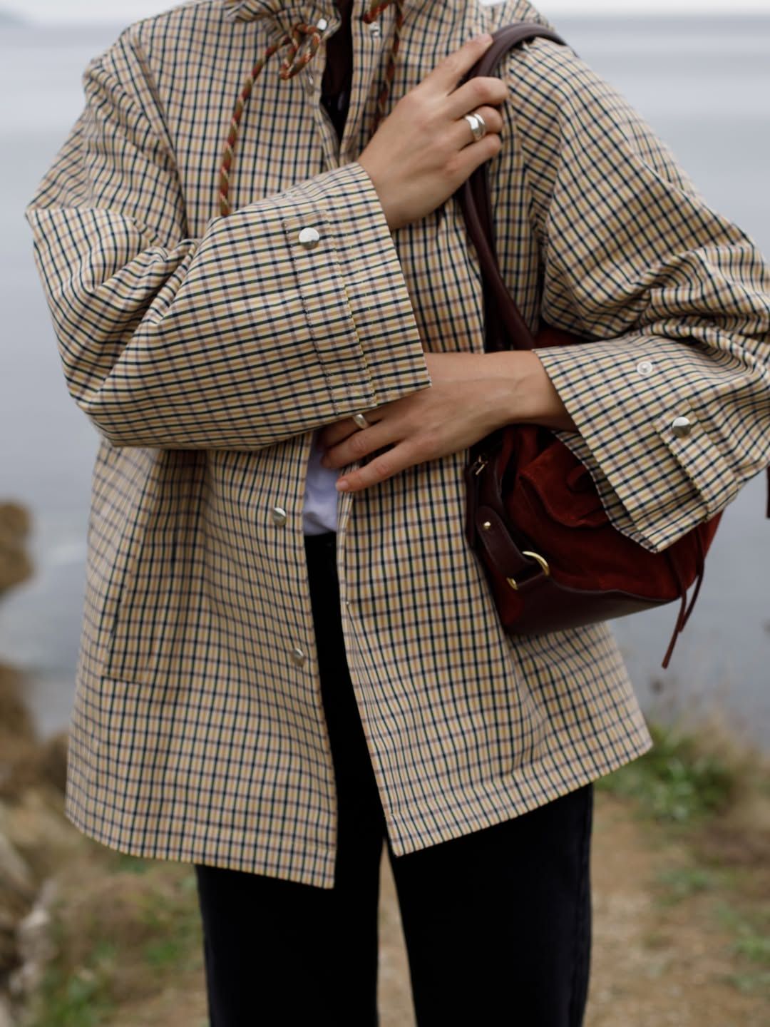 Jessica Skye wears a beige and black check jacket with rope drawstring details with a burgundy suede shoulder bag