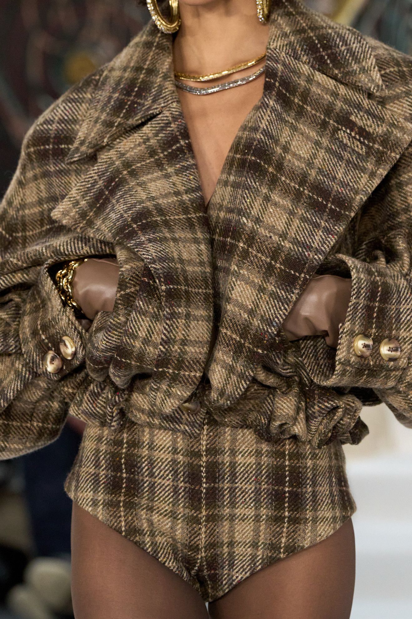 A model walks Paul Costelloe's A/W 27 runway in a cropped checked jacket in mustard and brown complete with matching micro shorts