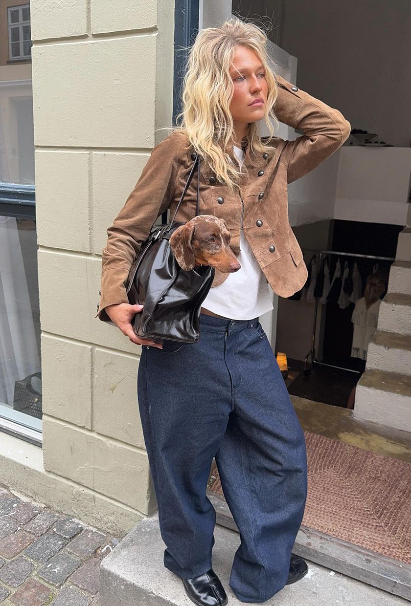 A woman standing outside wearing a suede band jacket with a white t-shirt, baggy jeans, and loafers.