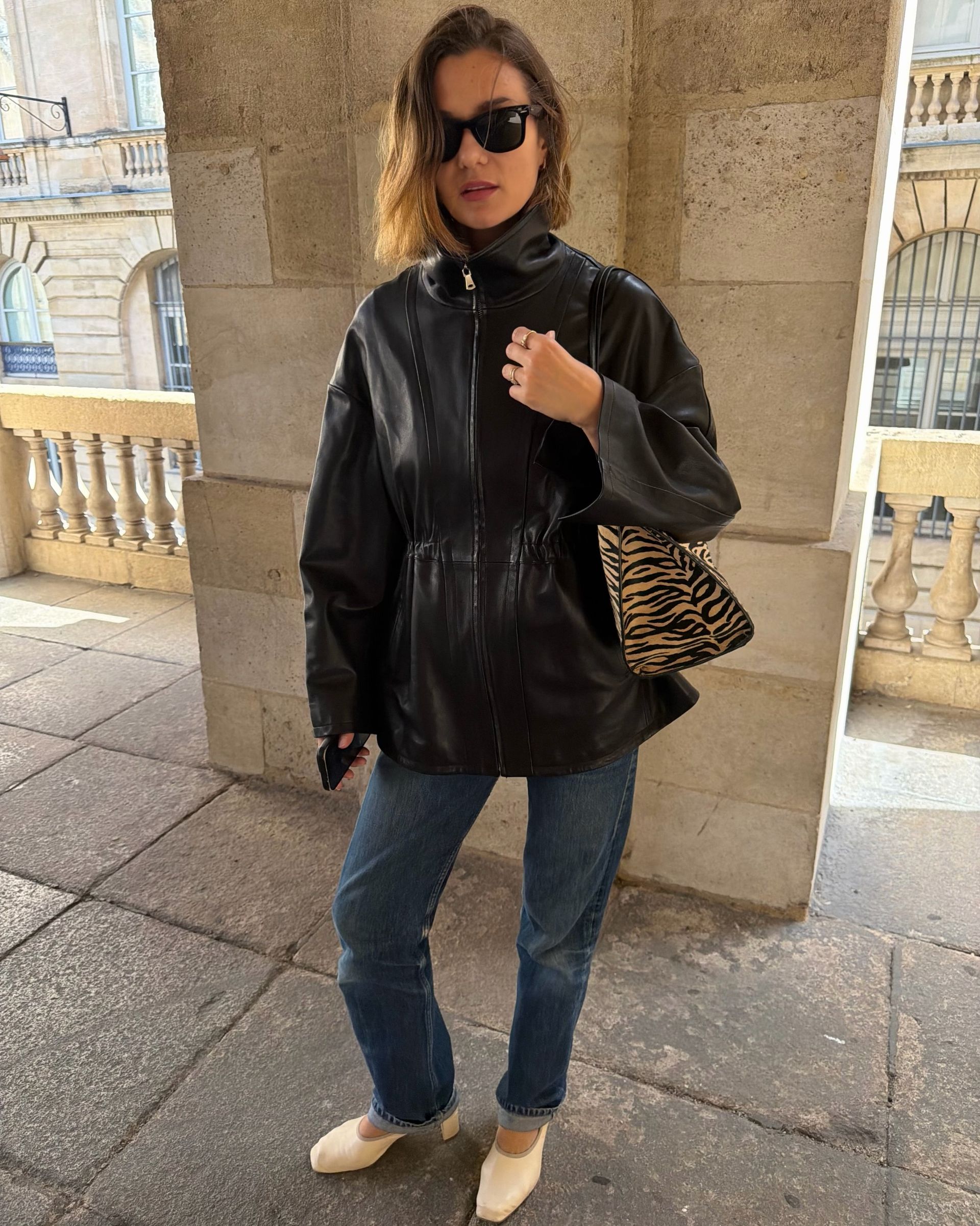 Influencer @annelauremais wears a black leather jacket with blue jeans, white heeled shoes and a tiger print bag.