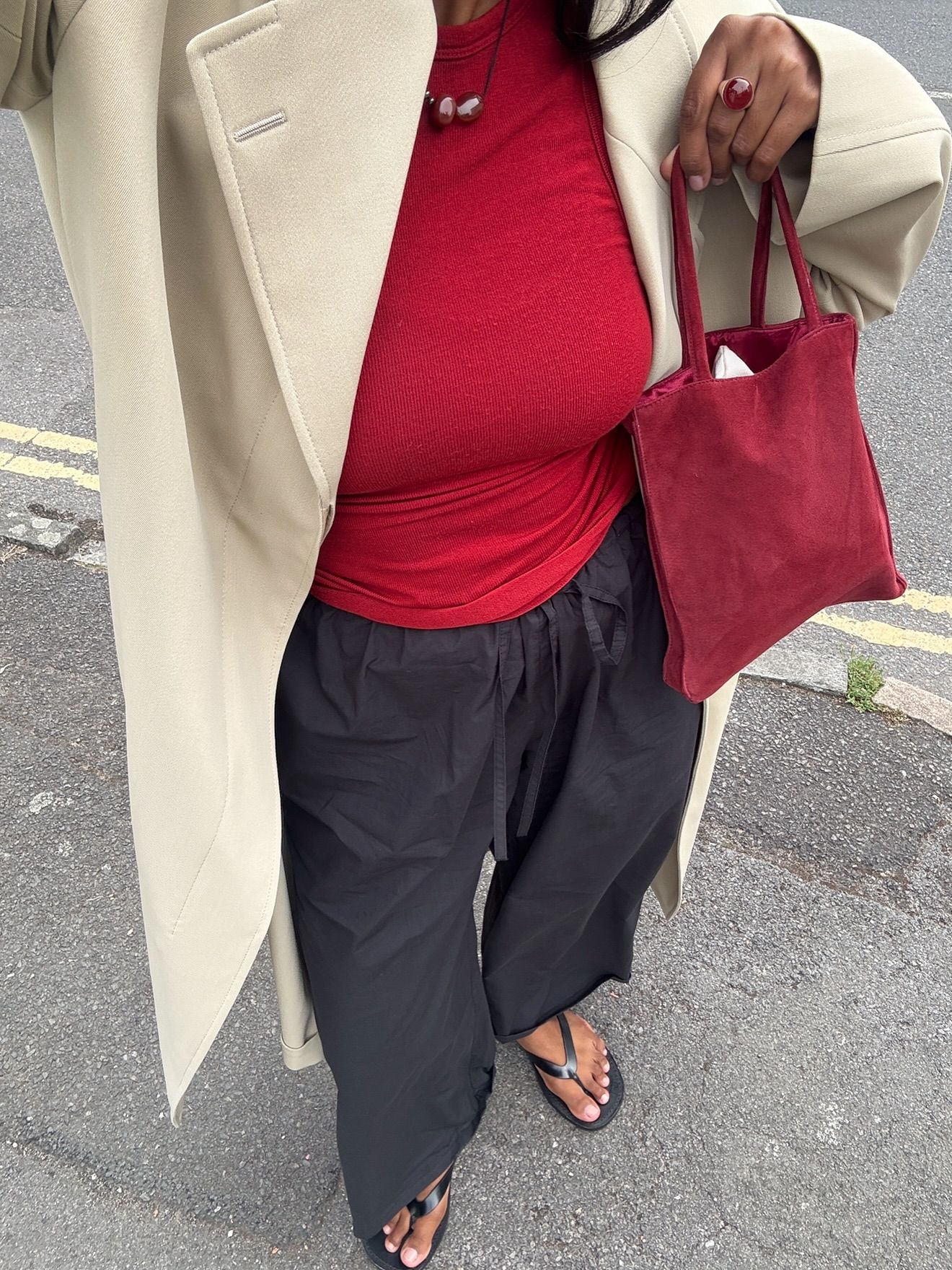 Monikh wearing natural pedicure with black flip flops, trousers, red top and trench coat