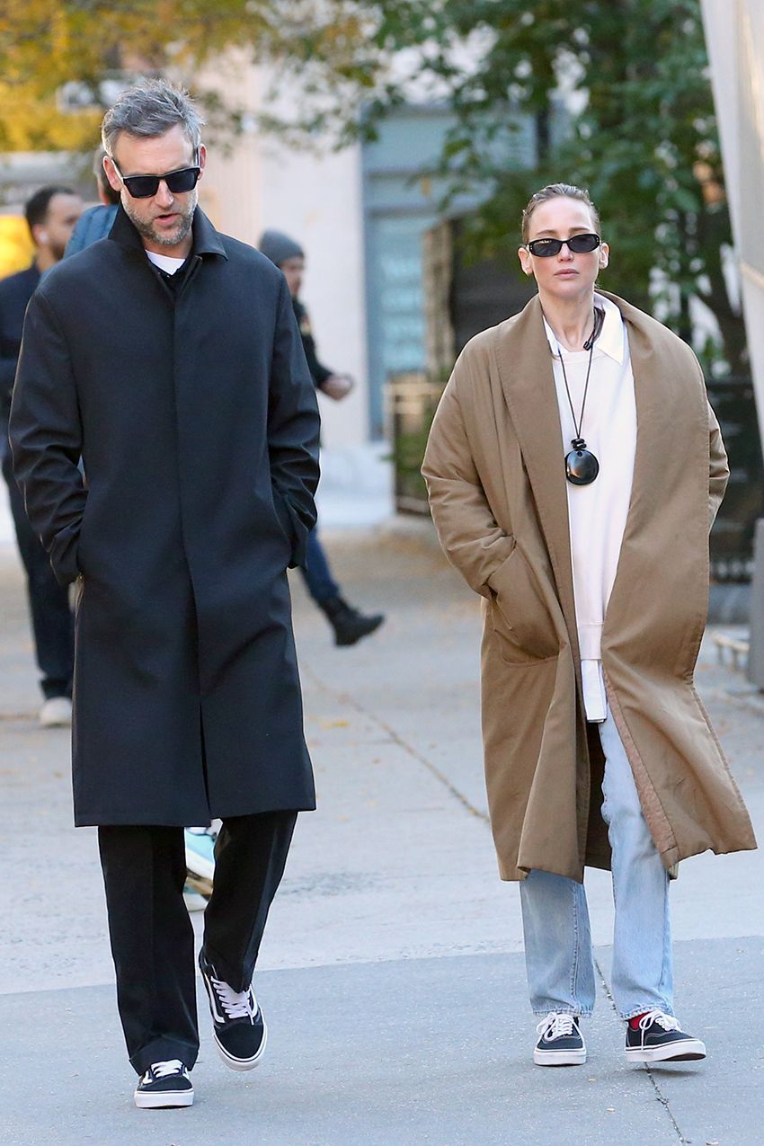 Jennifer Lawrence in NYC wearing a camel coat, large pendant necklace, white T-shirt, jeans, and Vans sneakers