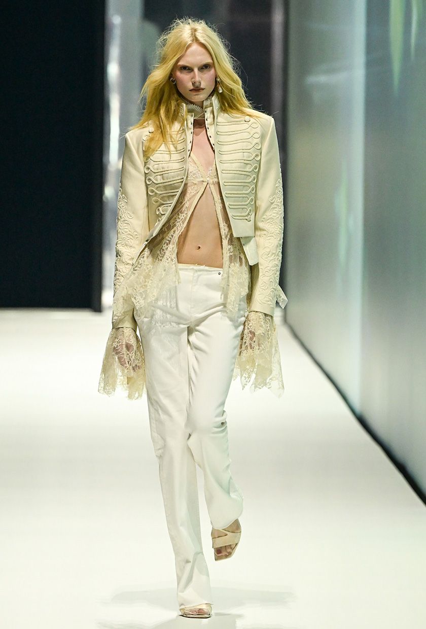 H&M model wearing a white jacket over a lace top with white low-rise jeans and white sandals.