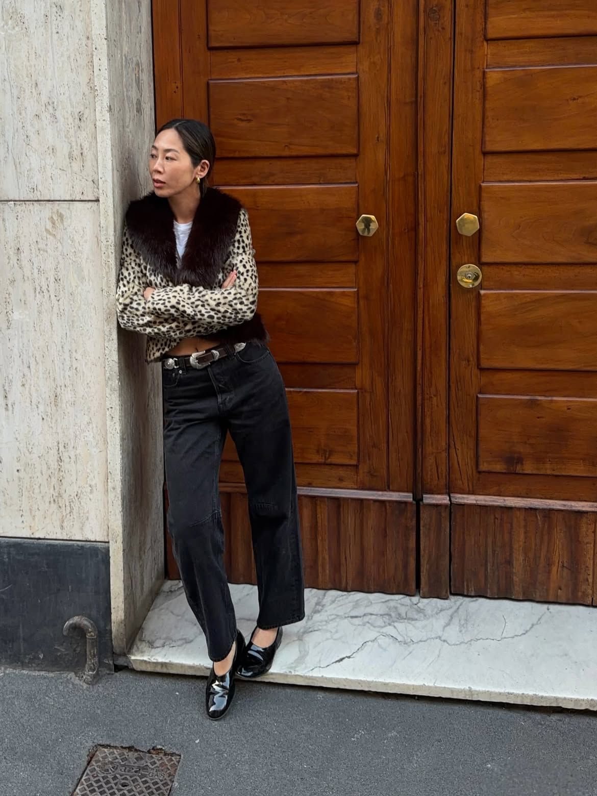 Woman wears a leopard print coat, jeans and flat shoes with a statement belt.