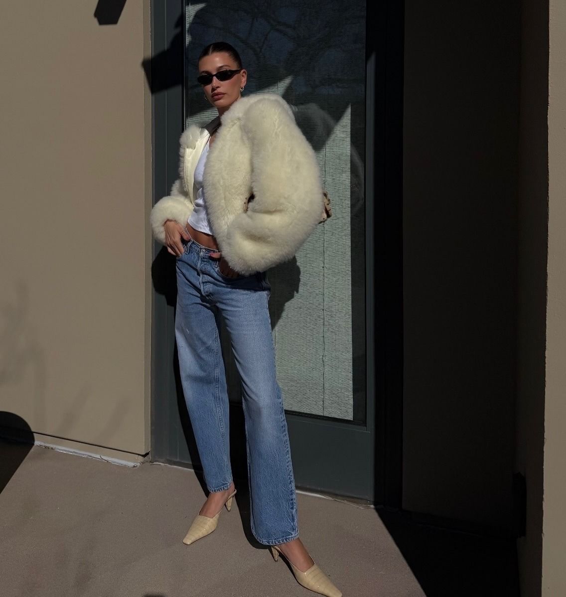 Hailey Bieber wearing a cream, fur jacket with vintage Levi's jeans and tan heels.