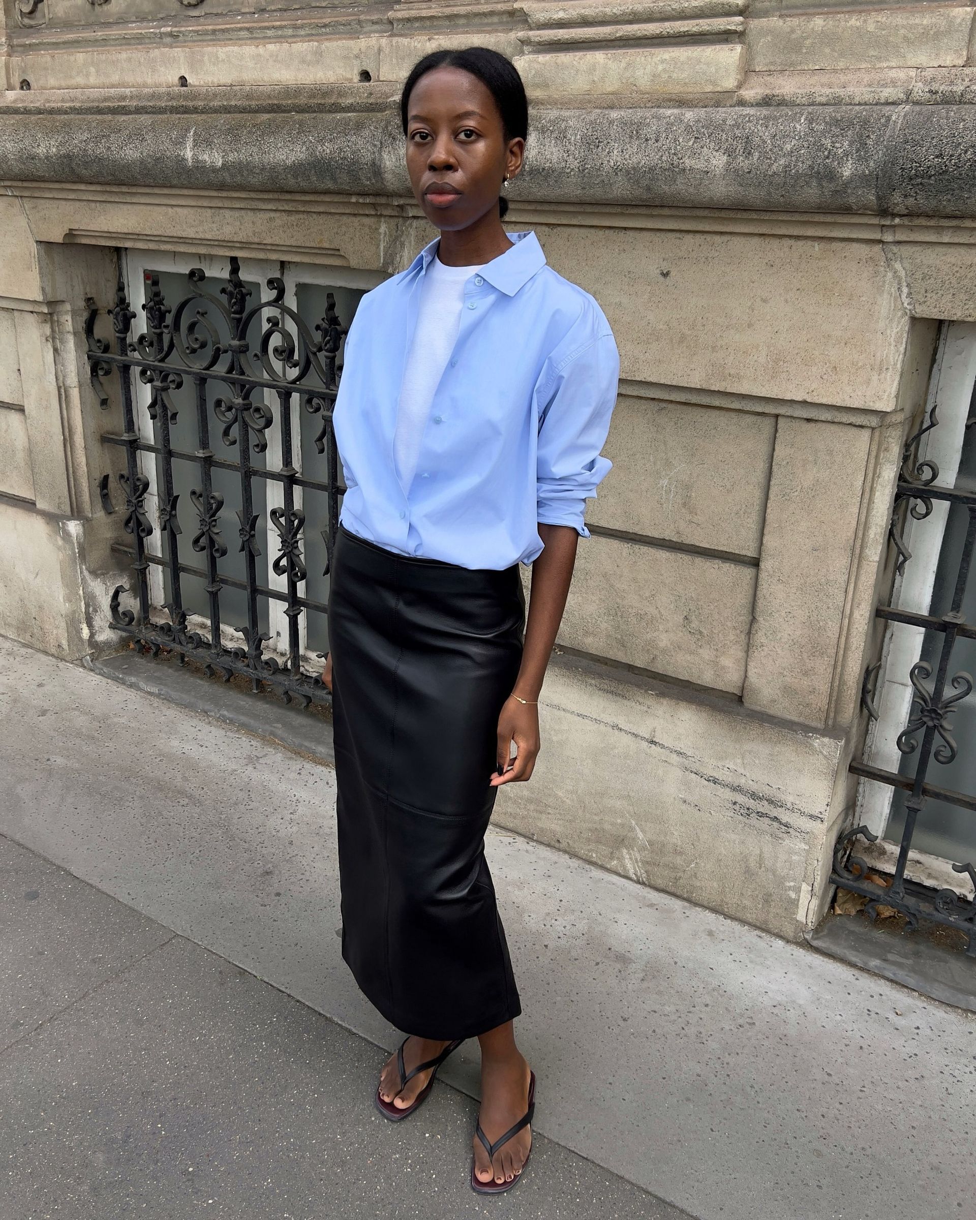 An image of an influencer in Paris wearing a black leather pencil skirt with a blue button-down shirt over top of a T-shirt