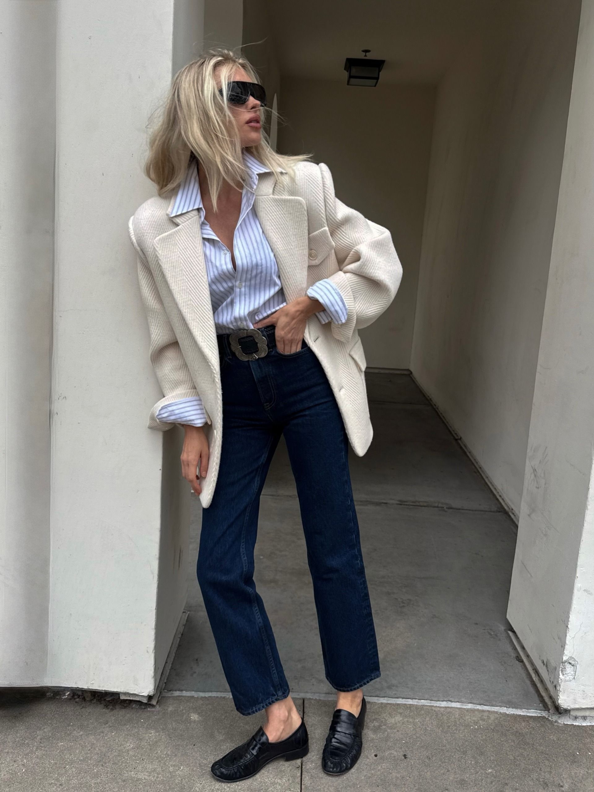 Elsa Hosk poses wearing dark wash cropped jeans with black loafers. She tucked a striped shirt into her jeans and layered a cream blazer on top.