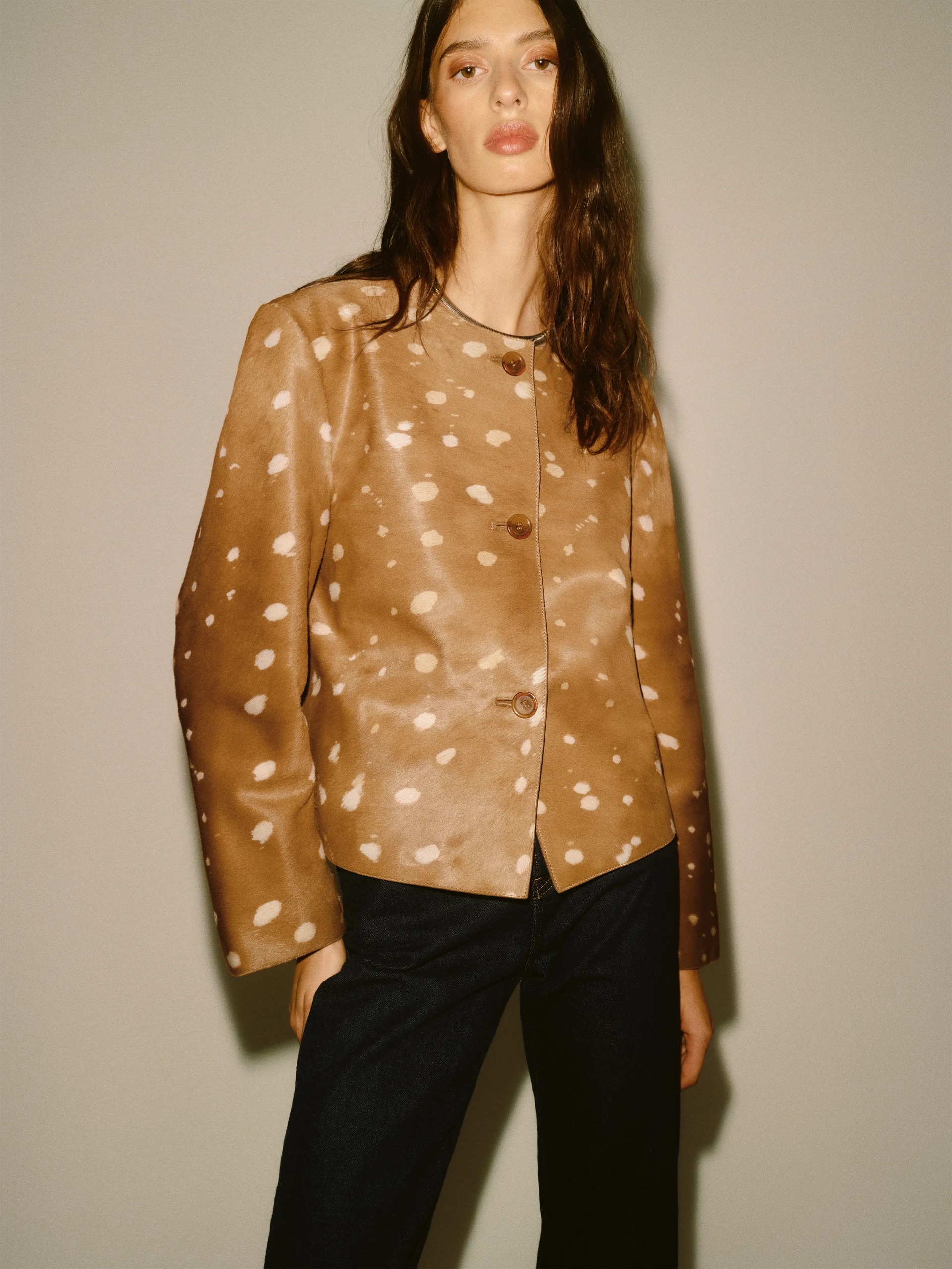 An image of a model wearing a light brown deer print jacket with black trousers from Reformation
