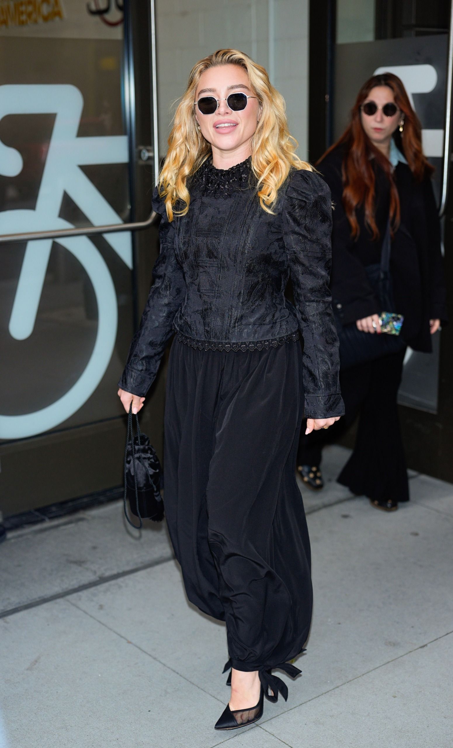 Florence Pugh steps out in New York wearing a black cinch-waist top with black balloon trousers and black mesh pointed-toe heels.