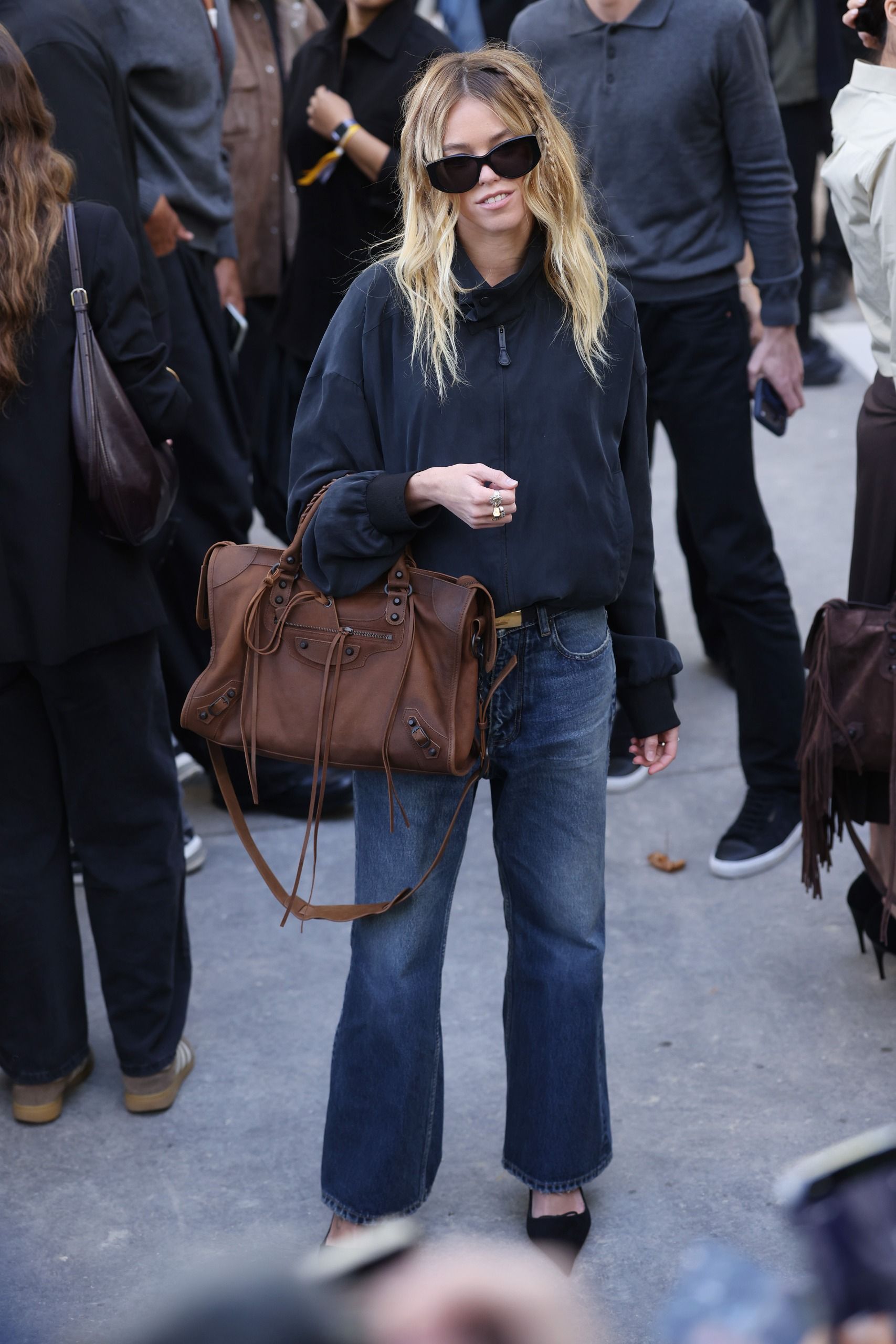 Milly Alcot wear bootcut jeans with a hip-length navy bomber jacket and a brown Balenciaga city bag.